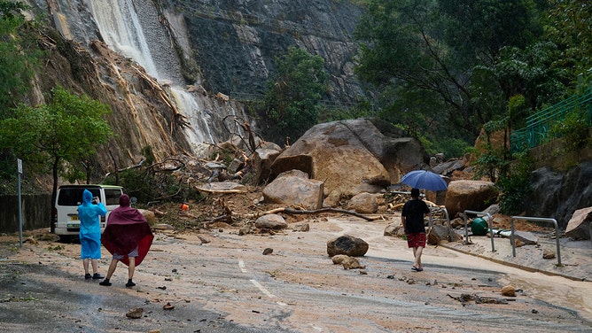 People watch a road blocked by stones at the scene of a landslide caused by torrential rain at Shau Kei Wan on September 8, 2023 in Hong Kong, China.