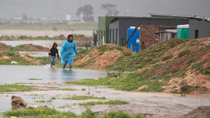A woman and child walks through water and mud during heavy flooding as a result of a storm in Sandvlei, close to Somerset West on September 25, 2023.