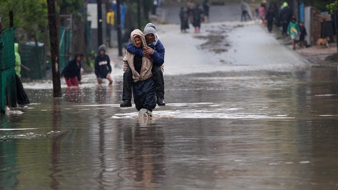 A man carries an elderly man across a flooded road during heavy flooding as a result of a storm in Sir Lowry's Village, close Somerset West on September 25, 2023.