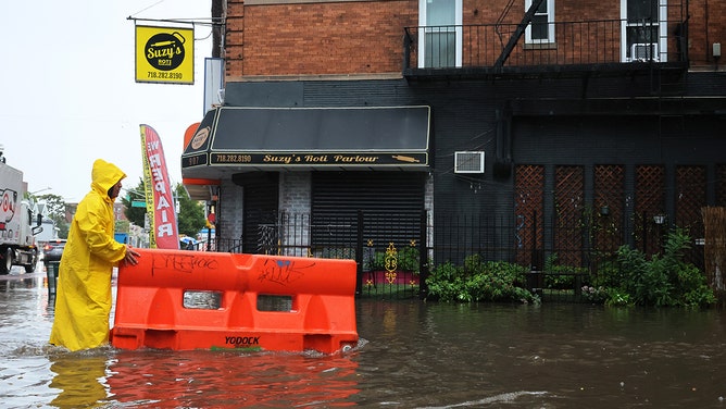 A person pushes a barricade floating on a flooded E 10th Street amid a coastal storm on September 29, 2023 in the Flatbush neighborhood of Brooklyn borough New York City.