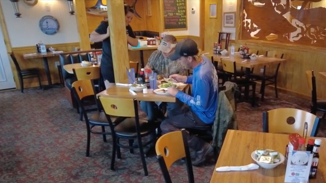 The two men sit at a nearly empty restaurant at Cape Hatteras as a waitress stands nearby.