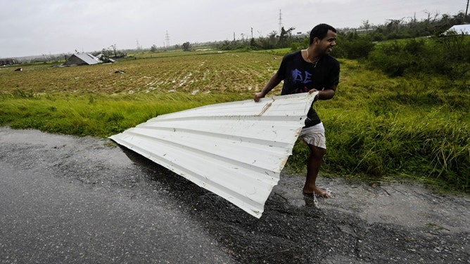 A man moves a piece of metal roof near destroyed tobacco drying houses in Puerta de Golpe, Cuba, on September 27, 2022, during the passage of hurricane Ian. - Hurricane Ian made landfall in western Cuba early Tuesday, with the storm prompting mass evacuations and fears it will bring widespread destruction as it heads for the US state of Florida. (Photo by ADALBERTO ROQUE / AFP) (Photo by ADALBERTO ROQUE/AFP via Getty Images)