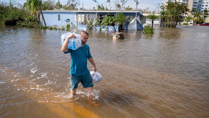 TOPSHOT - A man carrying bottled water wades through water in a flooded neighborhood in the aftermath of Hurricane Ian in Fort Myers, Florida, on September 29, 2022. - Hurricane Ian left a trail of devastation across Florida on Thursday with whole neighborhoods reduced to shattered ruins and millions left without power as US President Joe Biden warned of a high death toll. (Photo by Ricardo ARDUENGO / AFP) (Photo by RICARDO ARDUENGO/AFP via Getty Images)