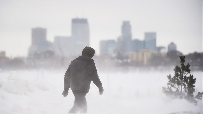 A man goes for a walk in front of the Minneapolis skyline at Bde Maka Ska Park during a snowstorm in Minneapolis, Minnesota, on February 22, 2023.