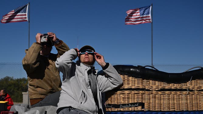 A hot air balloon crew, sitting next to gondola, watches the annular solar eclipse at the 51st Albuquerque International Balloon Fiesta in Albuquerque, New Mexico on October 14, 2023. (Photo by Patrick T. Fallon / AFP) (Photo by PATRICK T. FALLON/AFP via Getty Images)