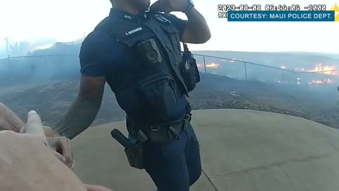 Officers assist a man during an evacuation, as the fires burn in the background. Aug. 8, 2023.