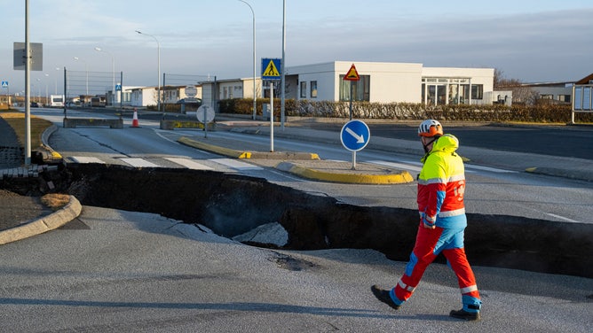 This photo taken on November 13, 2023 shows a member of the emergency services walking near a crack cutting across the main road in Grindavik, southwestern Iceland following earthquakes. The southwestern town of Grindavik -- home to around 4,000 people -- was evacuated in the early hours of November 11 after magma shifting under the Earth's crust caused hundreds of earthquakes in what experts warned could be a precursor to a volcanic eruption. The seismic activity damaged roads and buildings in the town situated 40 kilometres (25 miles) southwest of the capital Reykjavik, an AFP journalist saw. (Photo by Kjartan TORBJOERNSSON / AFP) / Iceland OUT (Photo by KJARTAN TORBJOERNSSON/AFP via Getty Images)