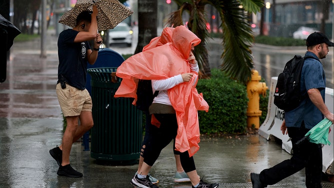 Pedestrians try to stay dry as rain inundates the area on November 15, 2023 in Miami Beach, Florida.