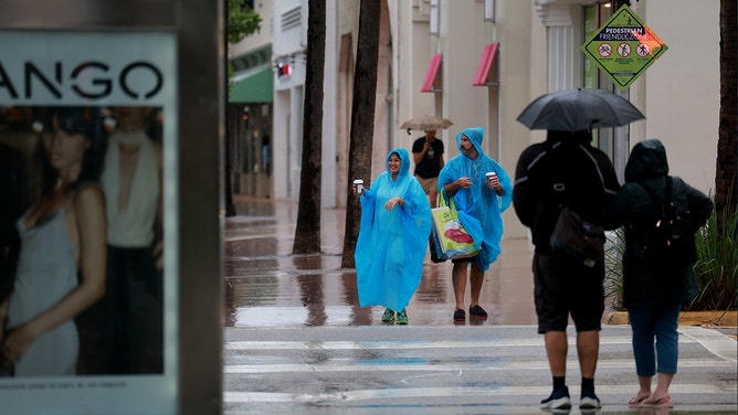Pedestrians try to stay dry as rain inundates the area on November 15, 2023 in Miami Beach, Florida.