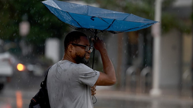 Wind blows a pedestrians umbrella inside out as he tries to stay dry as rain inundates the area on November 15, 2023 in Miami Beach, Florida.
