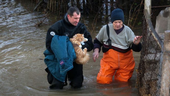 A rescuer carries a cat and helps a woman during an evacuation of residents of the flooded village of Pribrezhnoe in Crimea on November 27, 2023, following a storm. 