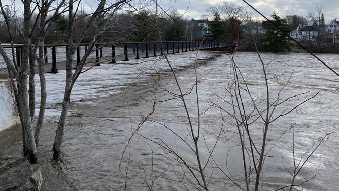 Waters rise below the Swinging Bridge that connects Bridge Street in Topsham, Maine, to Mill Street in the town of Brunswick. Dec. 19, 2023.