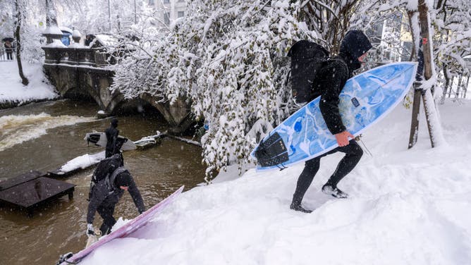 Two men carry their surfboards up the embankment at the Eisbach in the English Garden.