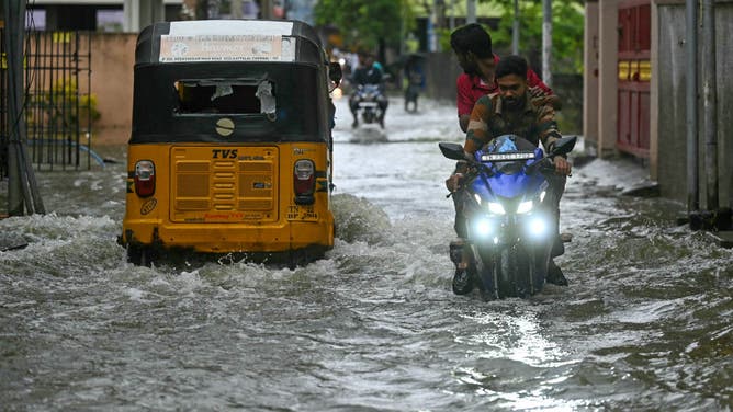 Commuters wade across a flooded street after heavy rains ahead of Cyclone Michaung's landfall in Chennai on December 3, 2023.