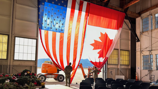 Augmentees assist 21st Civil Engineer Squadron personnel hang the American flag inside Hangar 123, the new location of the NORAD Tracks Santa Operations Center at Peterson Space Force Base, Colo., Dec. 20, 2023. Hangar 123 will provide more space and a more operational feel for the more than 1,000 volunteers who will enter the NTS Operations Center on Dec. 24 to answer phone calls from people around the world asking for Santa’s location. (Department of Defense photo by Michelle Martin)