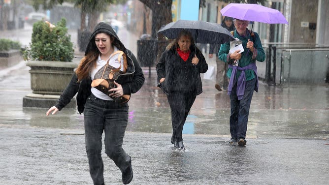People make their way across Broadway during a morning downpour in Santa Monica on December 20, 2023.