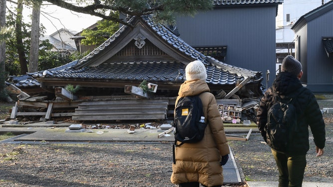 Residents walk past a collapsed building at the Jyuzo shrine in Wajima, Ishikawa prefecture on January 6, 2024, after a major 7.5 magnitude earthquake struck the Noto region on New Year's Day. Rescuers sifted through rubble on January 6 as focus turned to recovering bodies rather than finding survivors five days after a huge earthquake struck central Japan, with 98 people now confirmed killed. (Photo by Toshifumi KITAMURA / AFP)