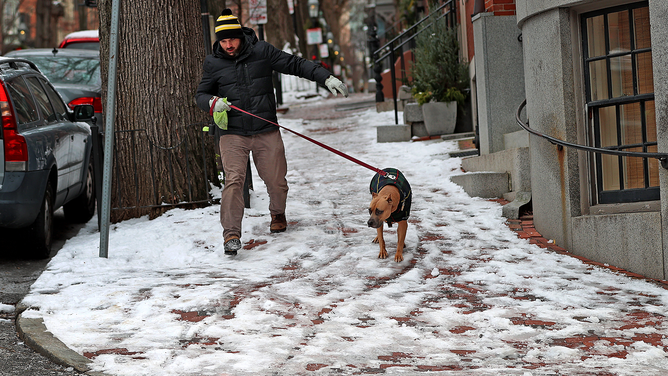 FILE - A man walks his dog on an icy and snowy Mt. Vernon Street sidewalk in Boston. (Photo by David L. Ryan/The Boston Globe via Getty Images)