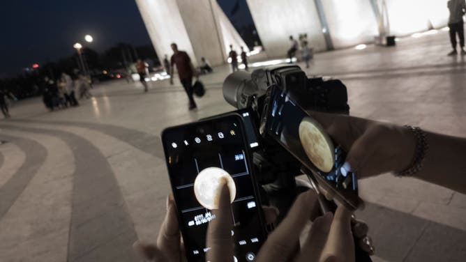 Photographers check an image of the moon, known as the Blue Moon, on their cell phones under the Azadi (freedom) monument in western Tehran August 30, 2023.