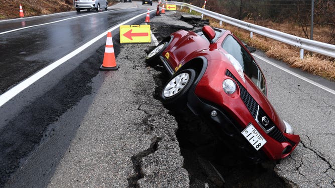 Traffic (L) passes along a newly paved road next to a car which remains stuck in the old pavement in the city of Anamizu, Ishikawa prefecture, on January 6, 2024, after a major 7.5 magnitude earthquake struck the Noto region on New Year's Day. (Photo by Toshifumi KITAMURA / AFP) (Photo by TOSHIFUMI KITAMURA/AFP via Getty Images)
