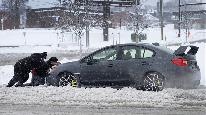 People help push a vehicle back onto the road after it became stuck in the snow on January 09, 2024, in Des Moines, Iowa.