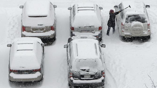 A woman clears snow off a car in a downtown parking lot in Portland, Maine