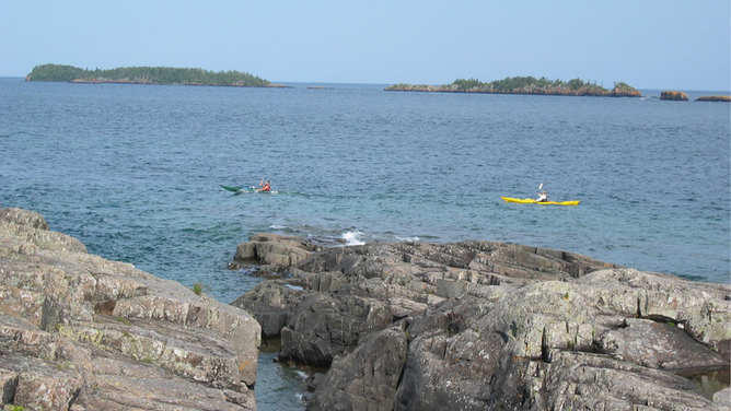 FILE - Two kayakers paddle past the rocky Lake Superior shoreline at Isle Royal National Park. 