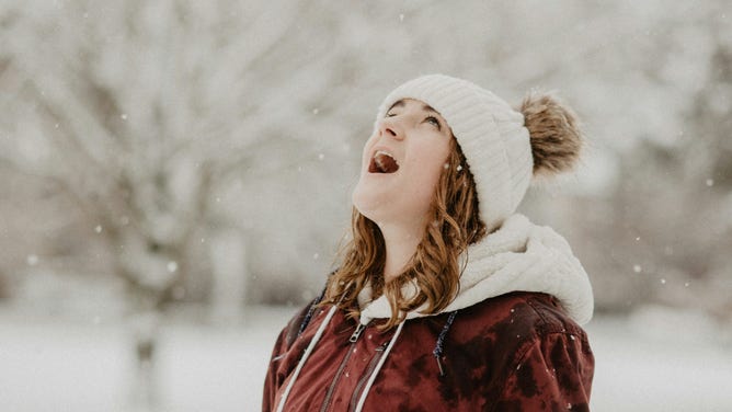 Woman catching snowflakes with mouth open.