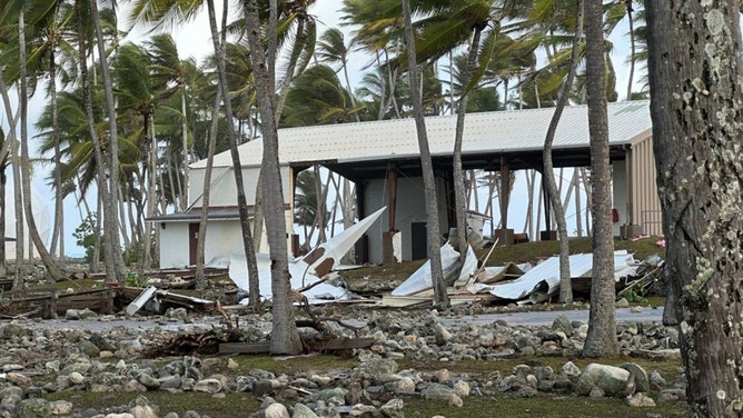 The Roi-Namur church steeple rests on the coral-strewn grounds on the opposite side of the Tradewinds Theater, background, from where it once stood. The steeple is the only part of the church that is recognizable.