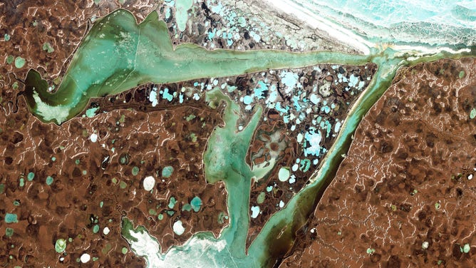 Imagem de satélite das baías Omulyakhskaya e Khromskaya ficam ao longo da costa norte da Sibéria. A terra ao redor das baías é pontilhada por lagos azul-petróleo brilhantes, que resultam da água liberada pelo degelo do permafrost.