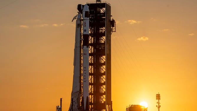 A colorful sunset behind the SpaceX Falcon 9 and Dragon at the launchpad at Kennedy Space Center.