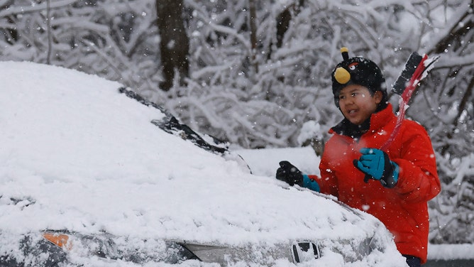 A boy cleans snow off a car in Tappan, New York, on February 13, 2024.