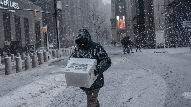 A pedestrian carries USPS boxes through the snow during a storm in New York, US, on Tuesday, Feb. 13, 2024.