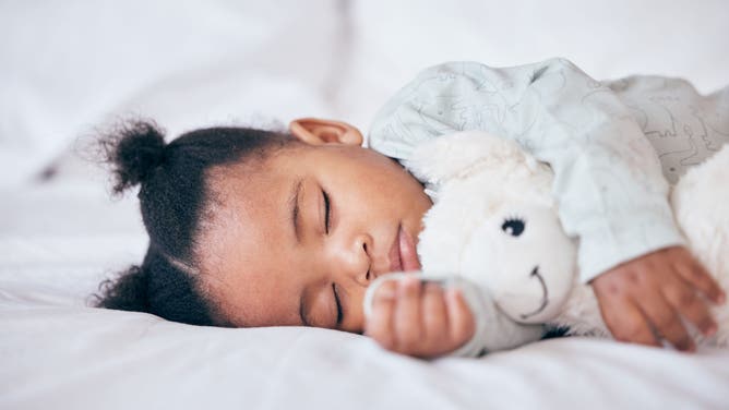 A baby girl sleeping with a teddy bear.