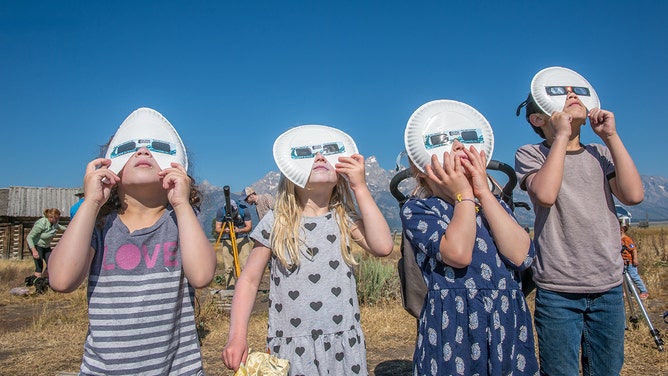 Group of children look up wearing eclipse glasses to watch Solar Eclipse, Grand Tetons National Park, Teton County, Wyoming.