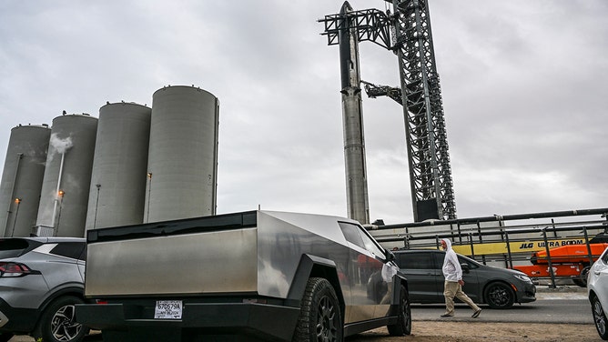 A man looks at a Tesla Cybertruck parked near the SpaceX Starship as it stands on the launch pad ahead of its third flight test from Starbase in Boca Chica, Texas on March 12, 2024.