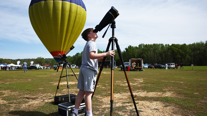 RUSSELLVILLE, ARKANSAS - APRIL 08: A youngster looks at the sun through binoculars at the Total Eclipse of the Heart festival on April 8, 2024 in Russellville, Arkansas. Millions of people have flocked to areas across North America that are in the "path of totality" in order to experience a total solar eclipse. During the event, the moon will pass in between the sun and the Earth, appearing to block the sun. (Photo by Mario Tama/Getty Images)