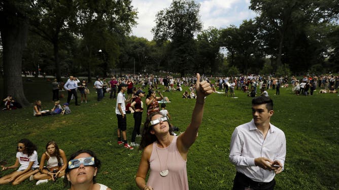 A woman wearing solar viewing glasses, center, holds up her thumb while looking at the sun during a solar eclipse at Central Park in New York, U.S., on Monday, Aug. 21, 2017.