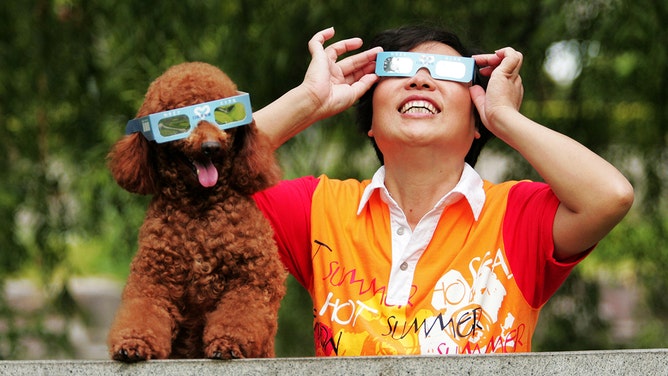 A woman observes the solar eclipse with her poodle on July 22, 2009 in Hangzhou of Zhejiang Province, China.