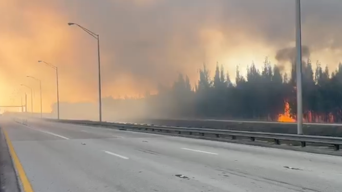 Flames are seen rising from a grass fire burning near Miami, Florida, on Sunday, April 14, 2024. Smoky conditions created limited visibility along nearby roadways.