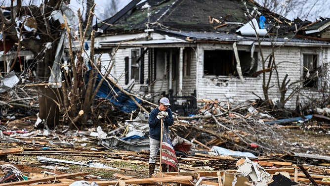 Tammy Beavers recovers a US national flag found in the debris of her destroyed home in Dawson Springs, Kentucky, on December 14, 2021, four days after tornadoes hit the area.