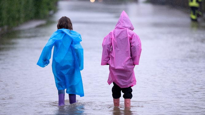 Two children in rubber boots walk across a flooded street in Dasing in the Swabian district of Aichach-Friedberg.
