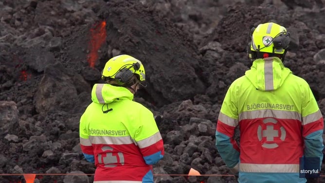 This image captured from a video recorded by Marco Di Marco shows two people standing in front of red-hot lava flowing over a main road to and from the evacuated town of Grindavik in Iceland after a volcanic eruption that began at the end of May 2024.
