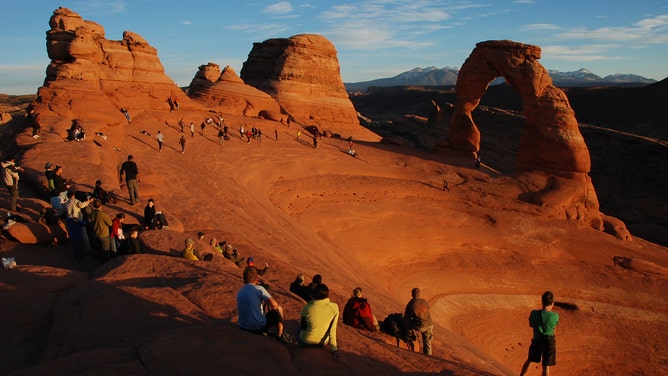 The Delicate Arch at sunset with park visitors nearby.