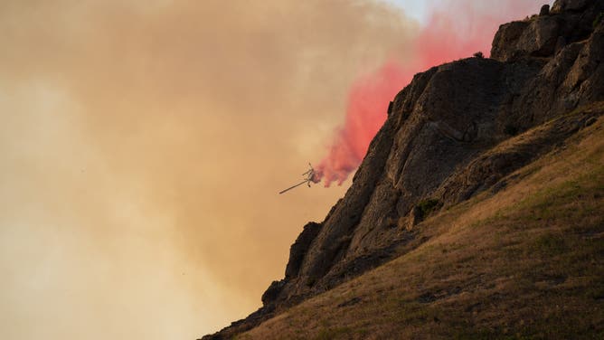 This image shows an airplane dropping fire retardant over the Sandhurst Fire burning outside Salt Lake City on Saturday, July 20, 2024.