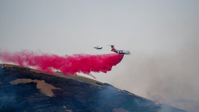 This image shows an airplane dropping fire retardant over the Sandhurst Fire burning outside Salt Lake City on Saturday, July 20, 2024.