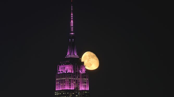 An 83 percent illuminated waning gibbous moon rises behind the Empire State Building lit in pink to mark Breast Cancer Awareness Month in New York City on October 2, 2023, as seen from Hoboken, New Jersey.