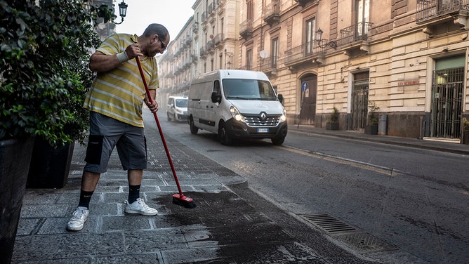 A man cleaning the pavement of Via Etnea from the volcanic ash that has fallen during the volcanic eruption that is causing inconvenience to pedestrians and vehicles on July 05, 2024 in Catania, Italy.