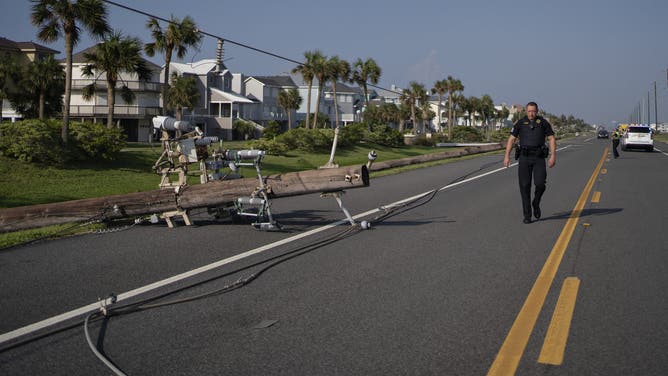 GALVESTON, TX - JULY 9: A police officer examines felled power lines along Termini-San Luis Pass Road in the wake of Hurricane Beryl on July 9, 2024 in the western part of Galveston island on Texas Gulf Coast about 50 miles from Houston. The category one hurricane, which made a direct hit on the city of Houston in Texas with 80 miles per hour winds at landfall, left more than two million people without power in the Houston area and beyond.