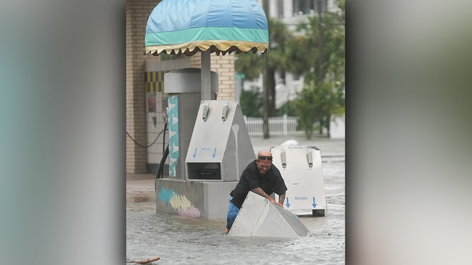 A man picks up trash cans that had floated off their stands at a self-serve carwash in Galveston as Hurricane Beryl wanes on Monday, July 8, 2024.